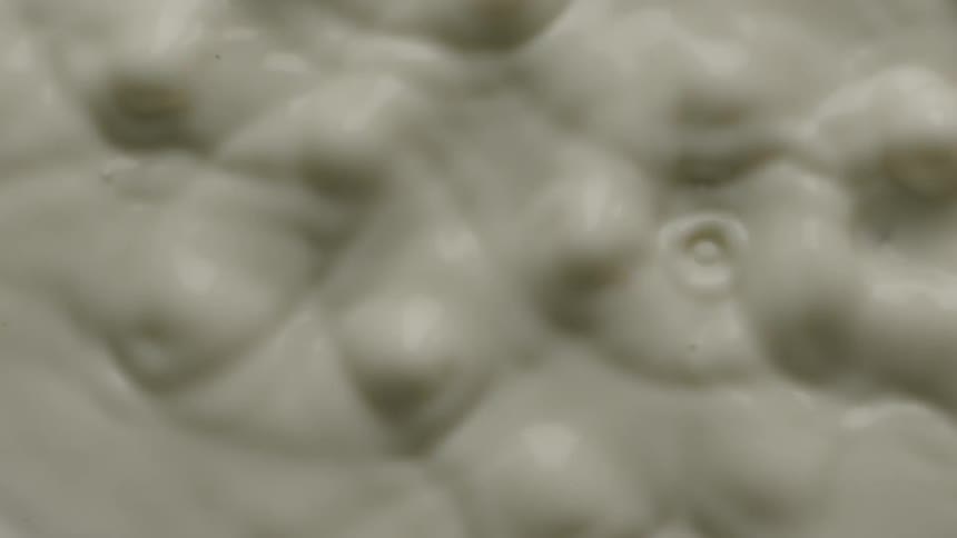The surface of a tan milky liquid can be seen rippling and splashing as it is being vibrating from below
