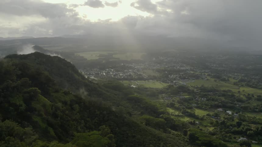 The sun streams through clouds onto a tree lined hillside and green valley