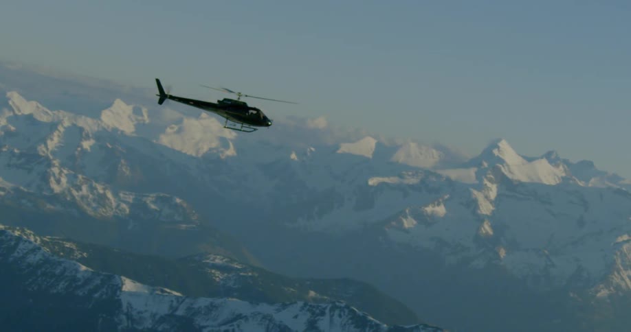 A helicopter flies over snow covered mountains