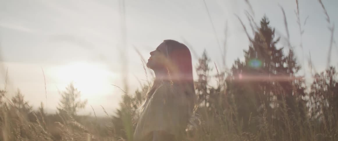 A woman stands in a field and looks towards the sky