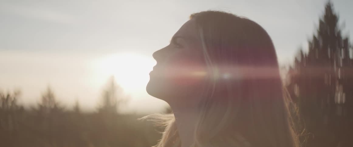 Woman stands outdoors looking at the sky as sun rises on the horizon
