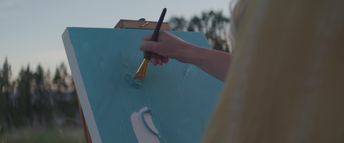 Woman paints canvas background with large paint brush in field