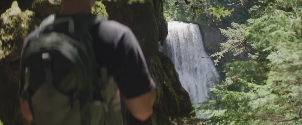A hiker watches water rush over a cliff