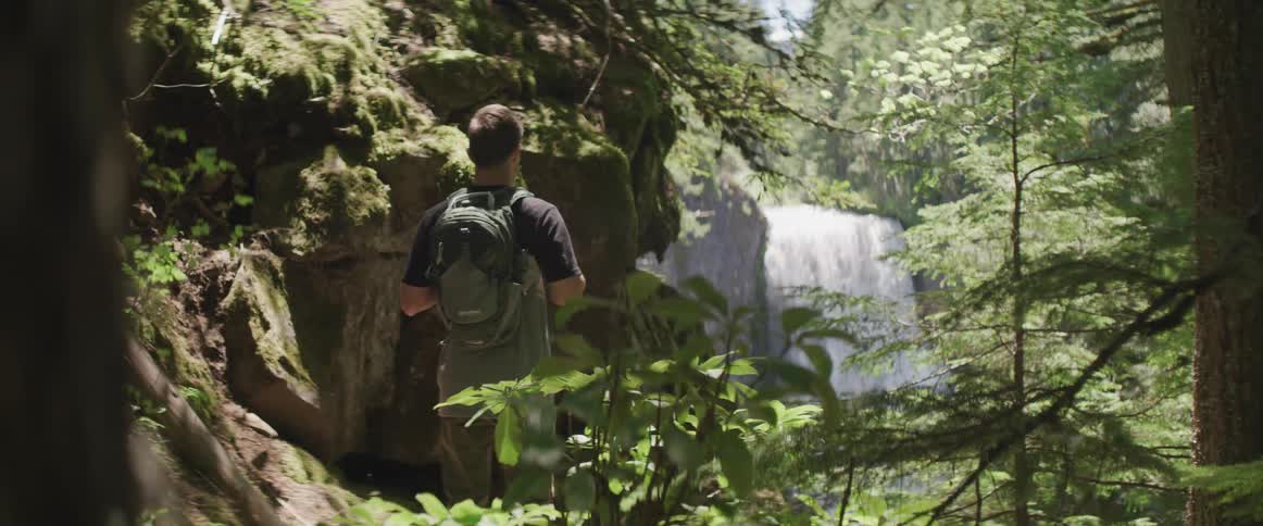 A hiker stops in the forest to watch a waterfall
