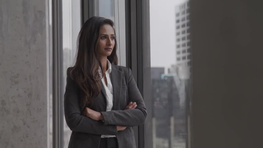 A young woman stands in an office building and looks out the window