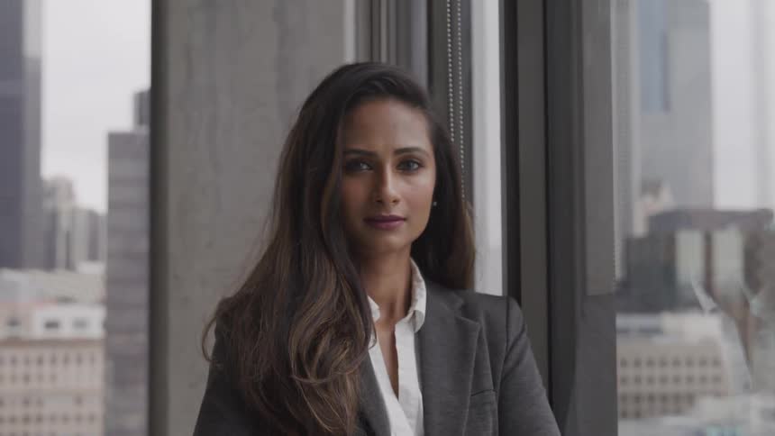 A woman in a suit poses next to a window in a high rise building