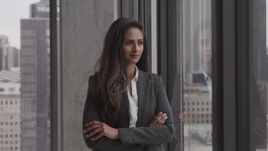 A young woman in business attire stares out of an office window