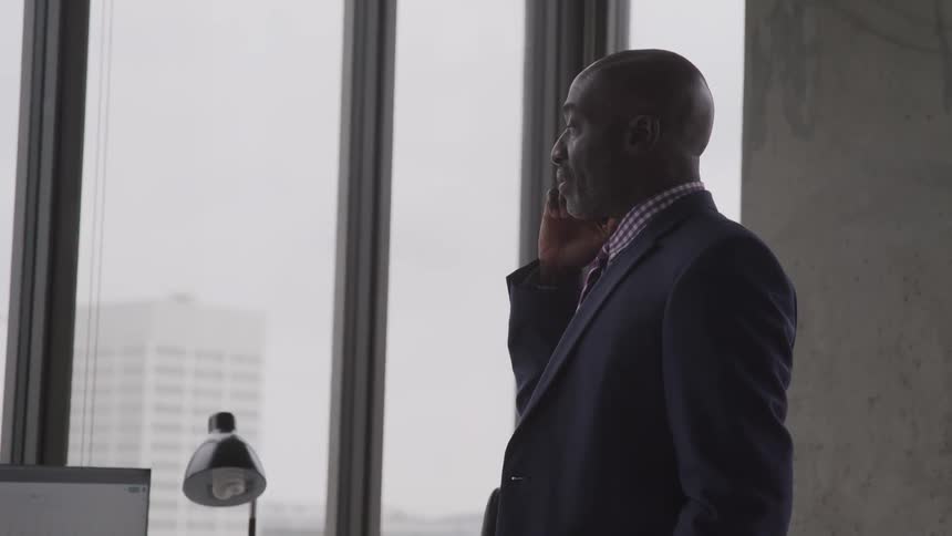 A man stands in his office and talks on his cellphone