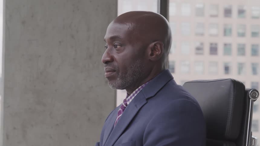 Black bald headed businessman wearing a suit sits on the chair in the office