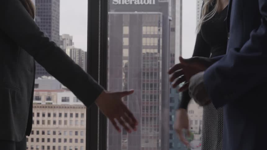 Three people all shake hands standing by a large office window