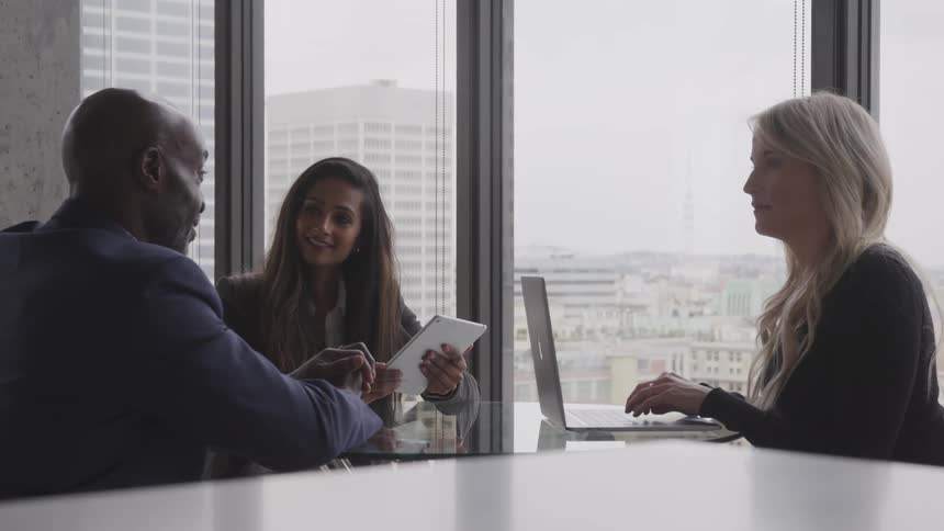 Three people are sitting at a desk and talking to eachother