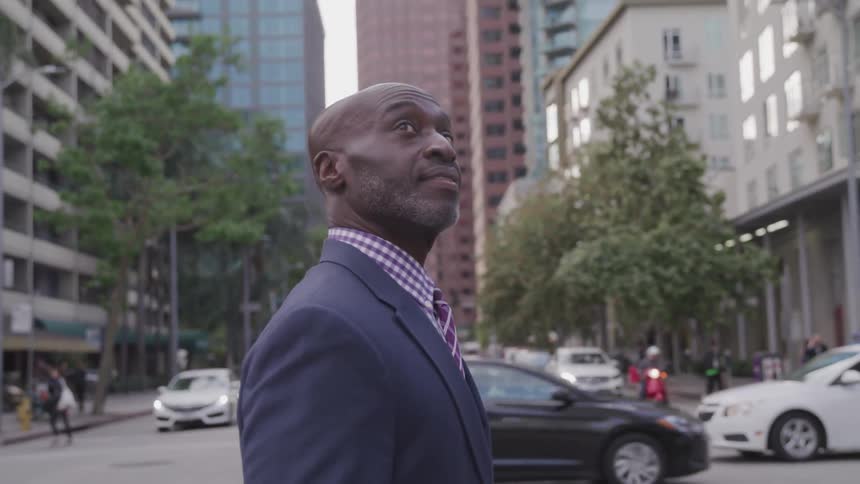 A man walks down a busy city street staring up at the skyscrapers