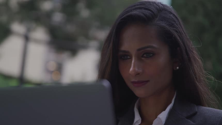A woman is smiling and looking at a laptop outdoors
