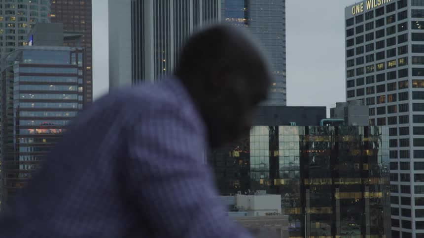 A black man stands outside with head bowed in the city
