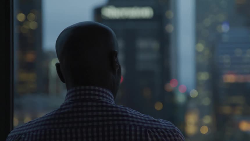 A man is looking out the window at the city at dawn