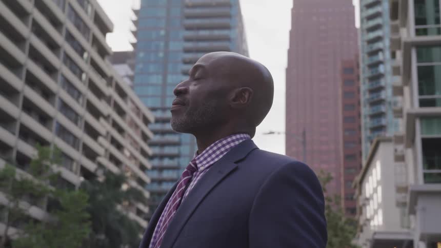 A man stands outside in a large city taking a deep breath