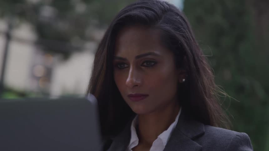 Businesswoman wearing a suit and sitting at the table uses a laptop at dusk
