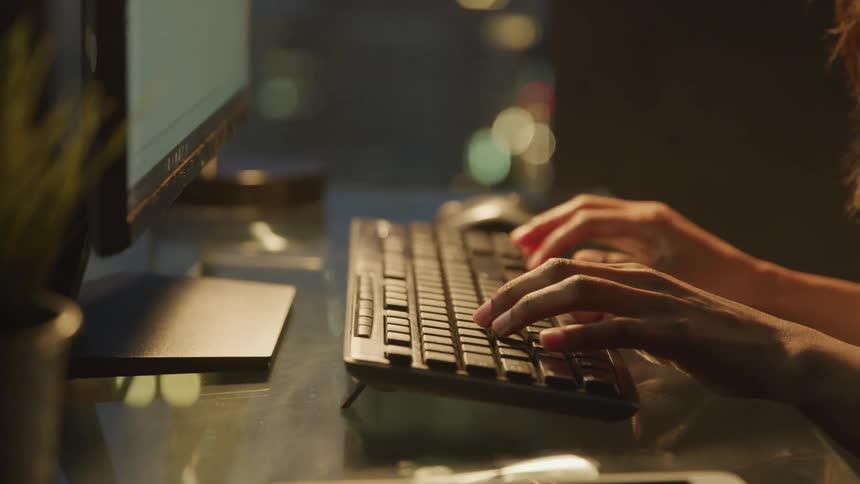 Black woman sitting at the desk types on the keyboard in the office at night