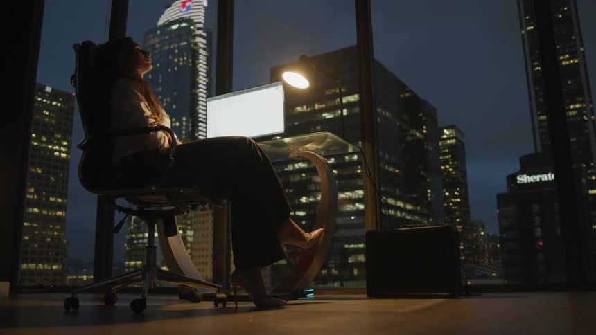 Businesswoman sitting at the glass desk relaxes in the office at night