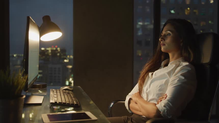 A woman with red hair sitting back into her chair before leaning in to her desk and typing something