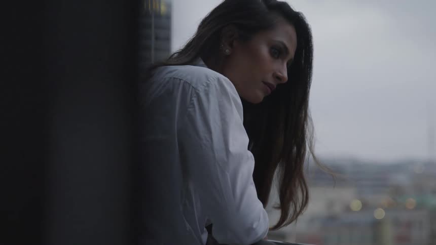 Business woman rests her elbows on banister on the office balcony at dusk