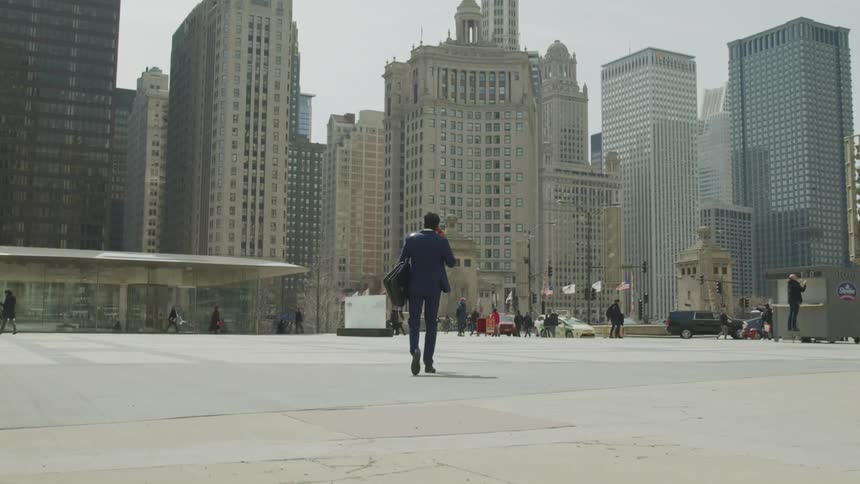 A man walks the open pathway toward large city buildings