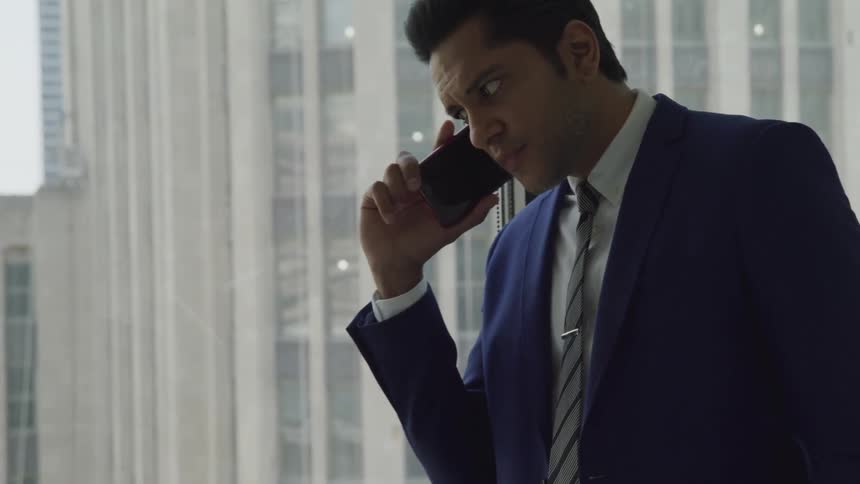 Businessman in a blue suit walks and talk to someone on the phone in the office