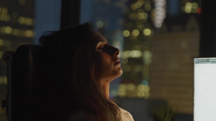 A woman sits with her eyes closed in front of her computer