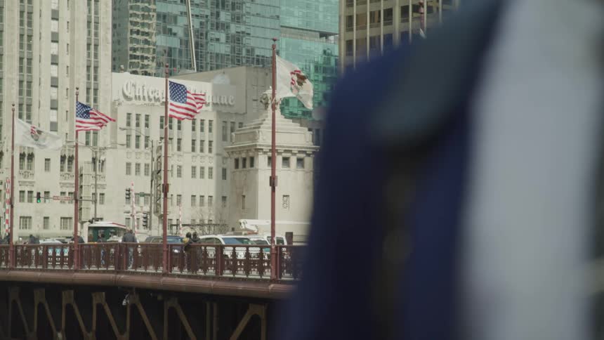 A man in a suit stands near a bridge in the city