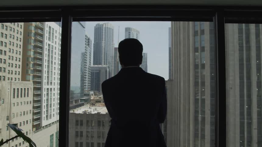Businessman looks out the window at the tall buildings of the city in the office