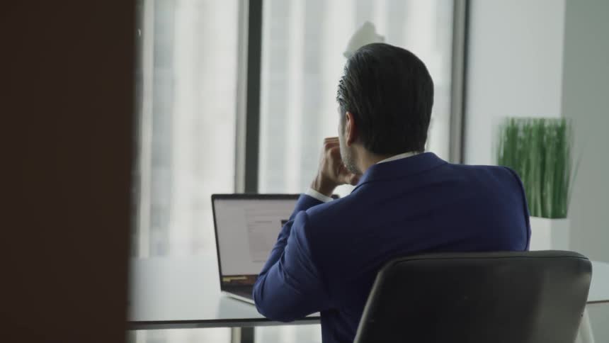 A man is sitting at a desk and looking at a laptop