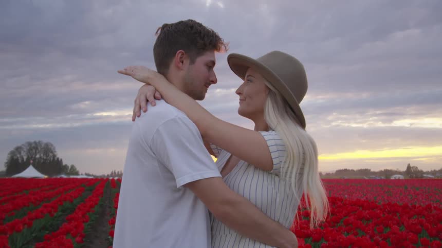 A man and woman embracing in a field of red flowers on a cloudy day
