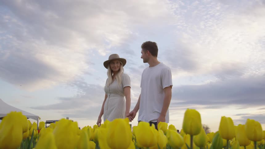 A woman and man are holding hands and walking through a field