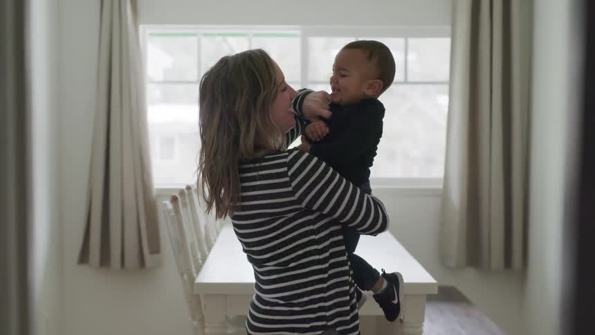 A mom holds her toddler and tickles him