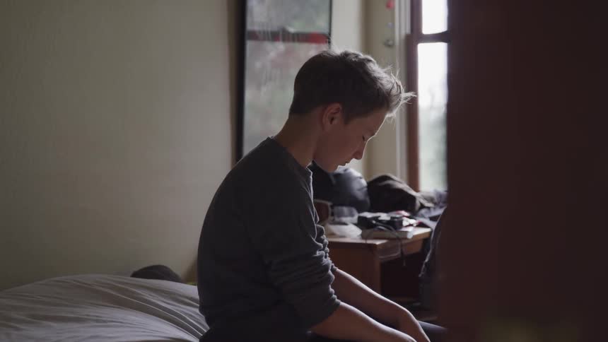 A boy sitting down on his bed with his eyes close