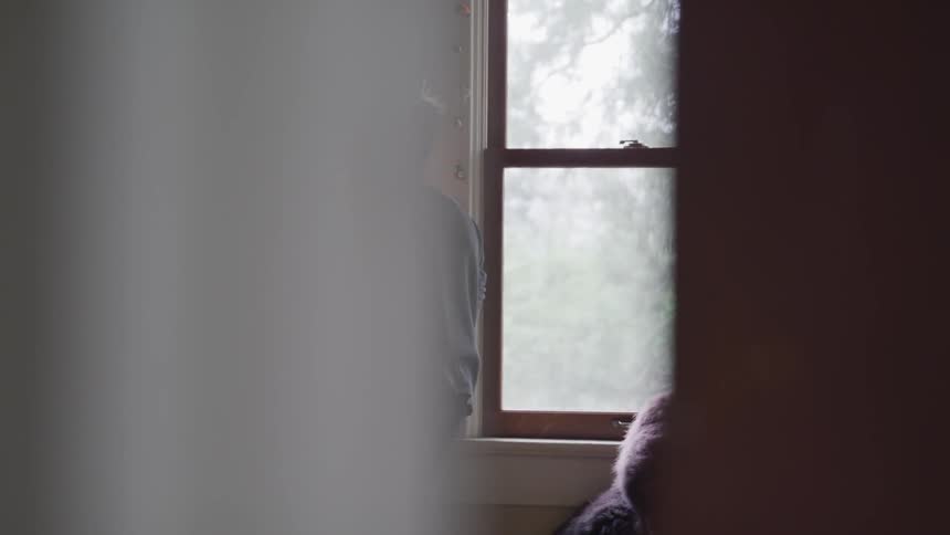A boy stands next to his bedroom window and looks outside
