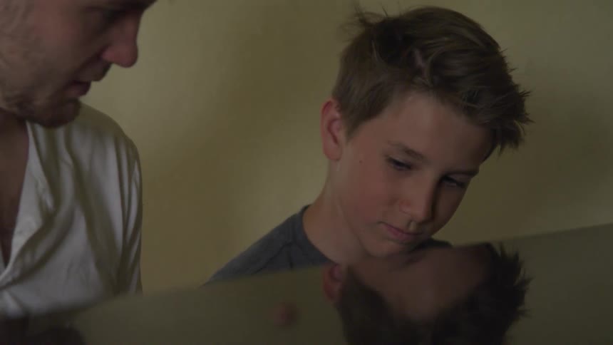 Father teaches son how to play a piano indoors during the day