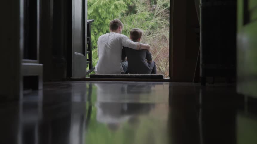 A teenage boy gives a younger boy a hug while they sit on the outside steps
