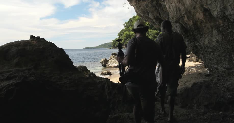 Two men hiking out of a cave near a beach