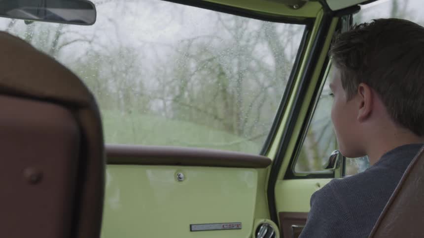 Boy smiles toward driver from passenger seat while driving through wilderness