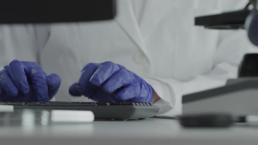 A person working in a lab types on a keyboard while wearing blue latex gloves