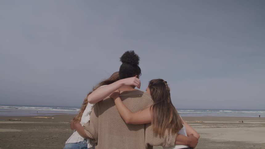 Three women in the beach stand hugging and laughing