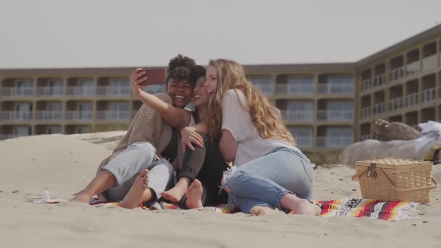 Three teenagers sit on a beach and take a selfie