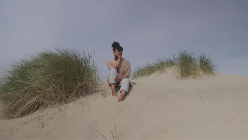 A young girl sits in the sand and looks off in to the distance