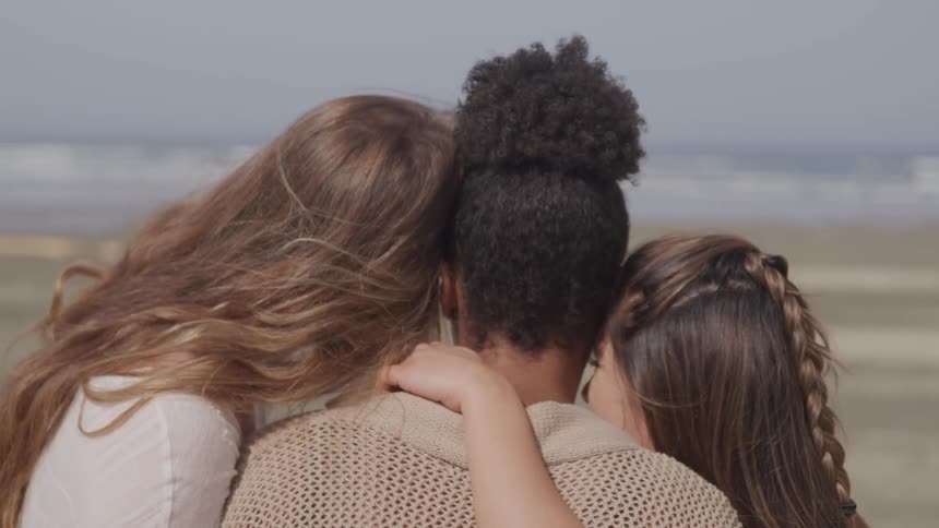 Three teenage girls hug while standing on the beach