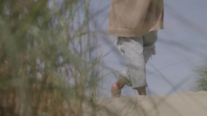 A person barefooted standing on the sand with plants in the foreground