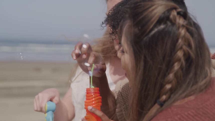 Three women bubbles with bubble wands and gun while standing on the beach