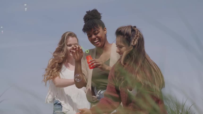 Three females stand outdoors laughing and blowing bubbles