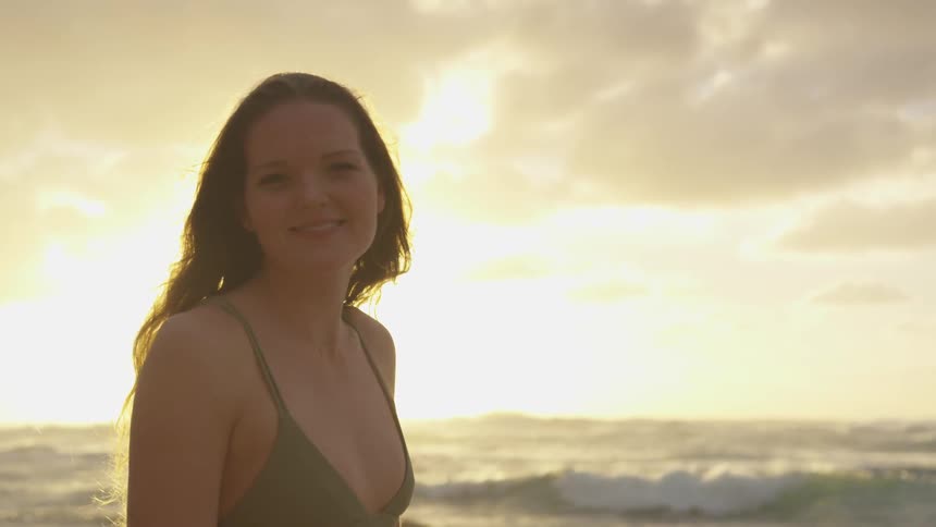 A woman poses on the beach at sunrise