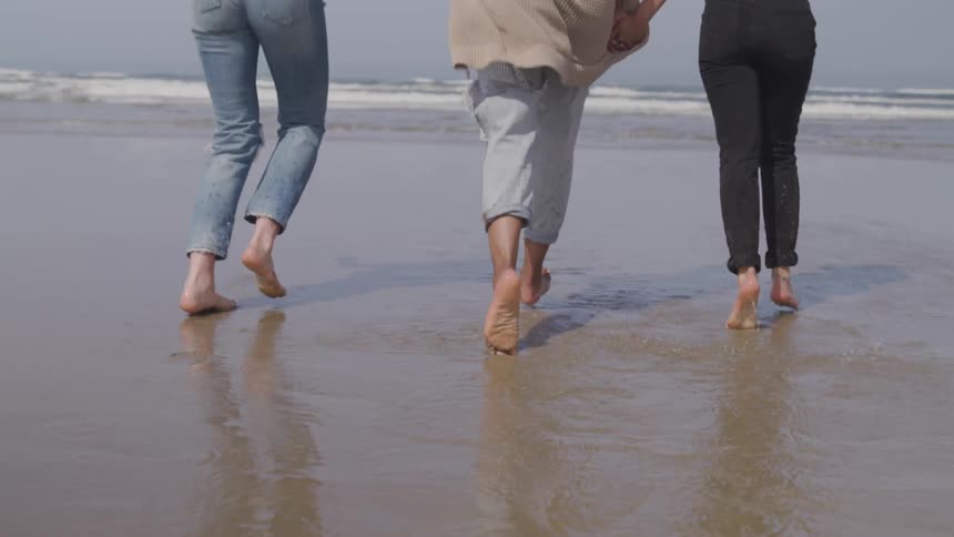 Three people walk and job barefoot across the sand toward the ocean